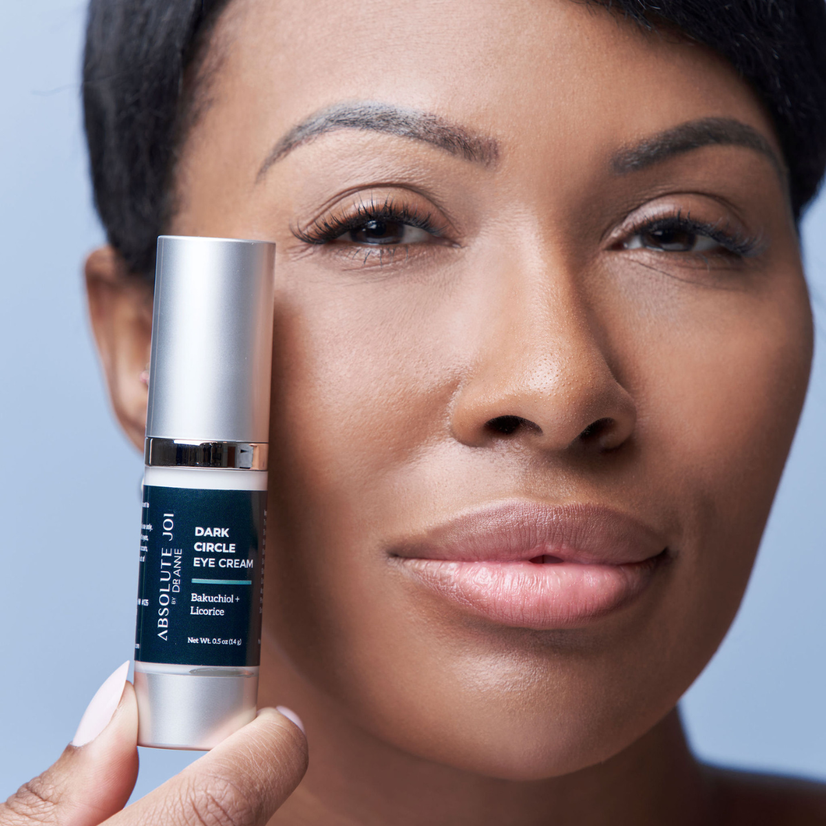 Woman holding a bottle of eye cream against a blue background