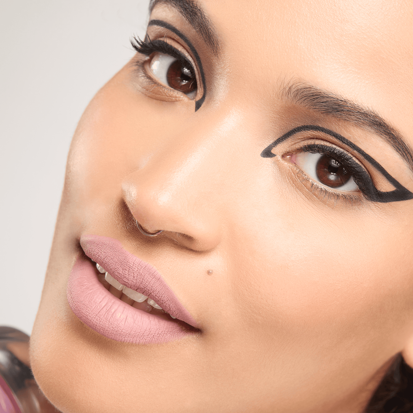 Close-up of a woman's face with cat-eye makeup on a neutral background