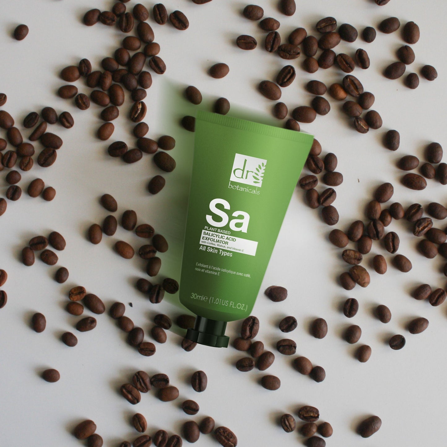 Green skincare product tube surrounded by coffee beans on a white background