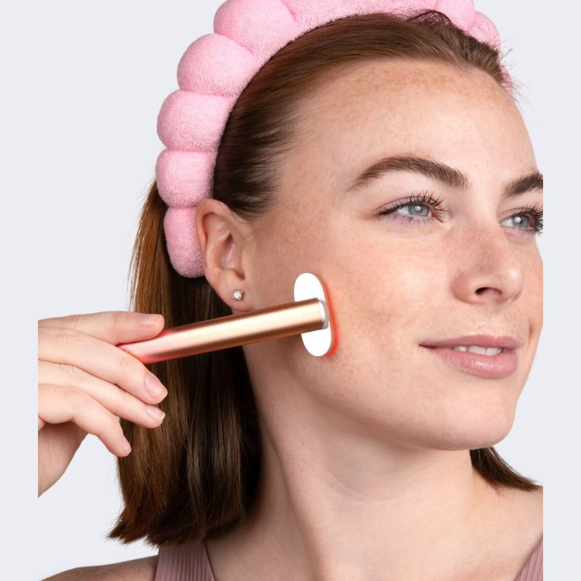 Woman applying makeup with a brush, wearing a pink headband.