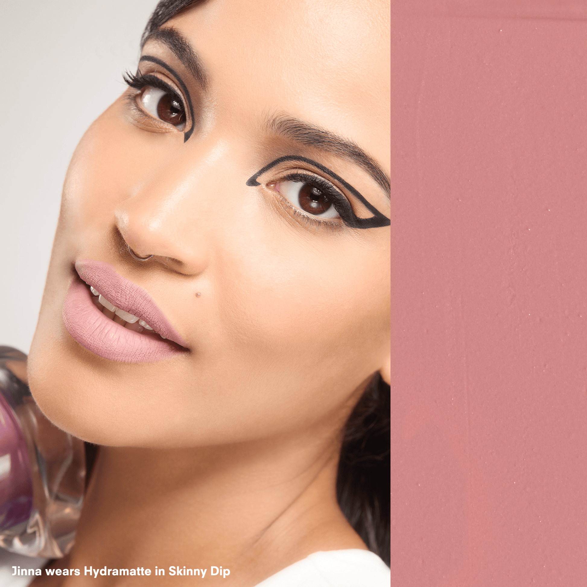 Close-up of a woman's face with makeup, specifically eyeliner, on a pink background.